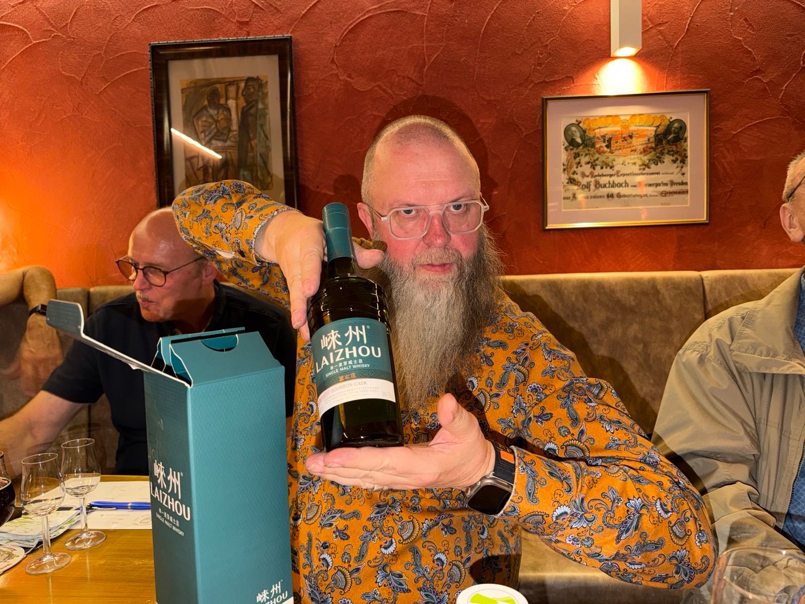 Ein Clubmitglied präsentiert am Tisch im Körnergarten Dresden eine Flasche Laizhou Single Malt, daneben die türkisfarbene Geschenkverpackung